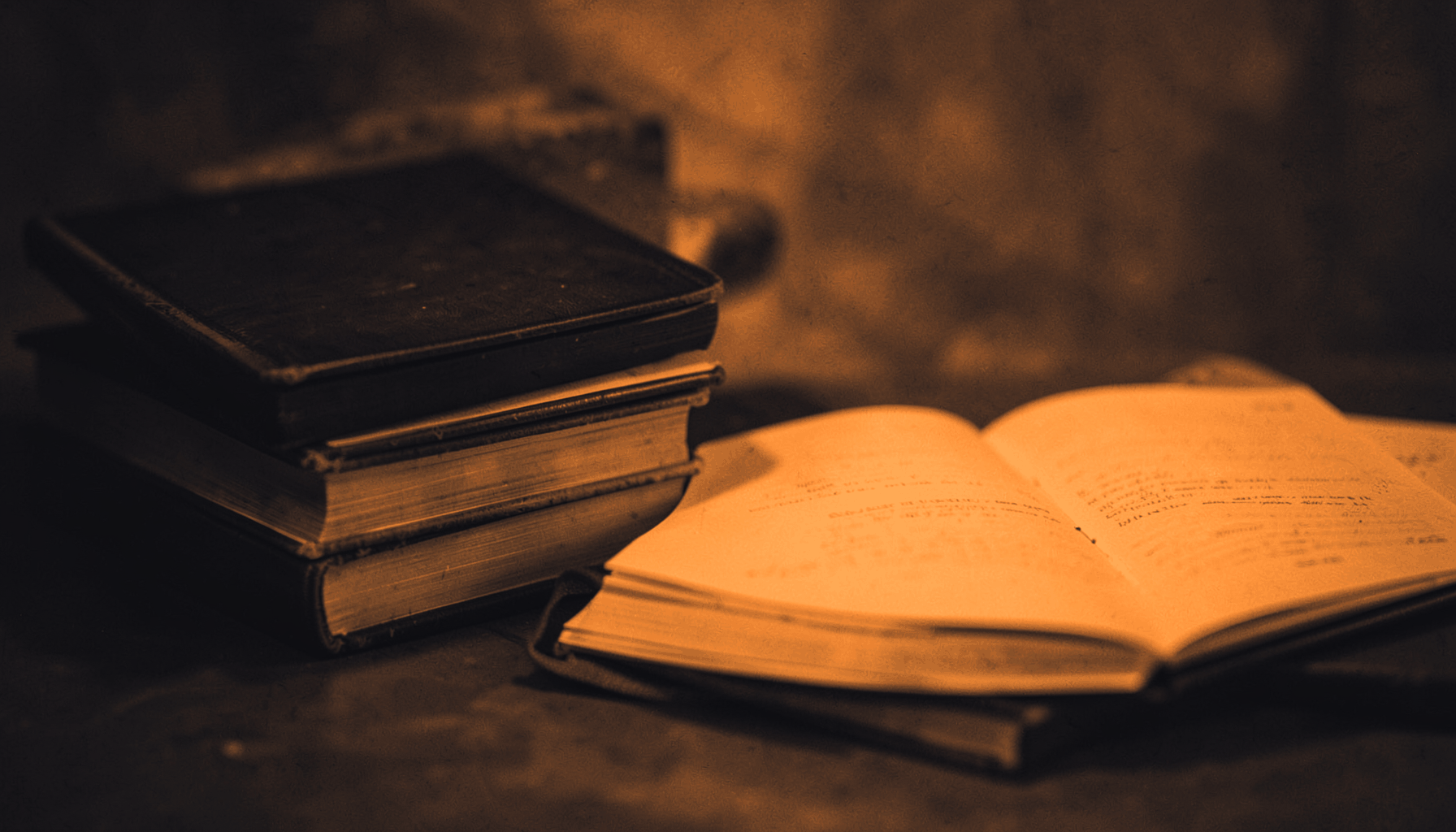 A duotone photograph in warm orange and deep charcoal tones showing a stack of closed books beside an open notebook, evoking a quiet, thoughtful mood.