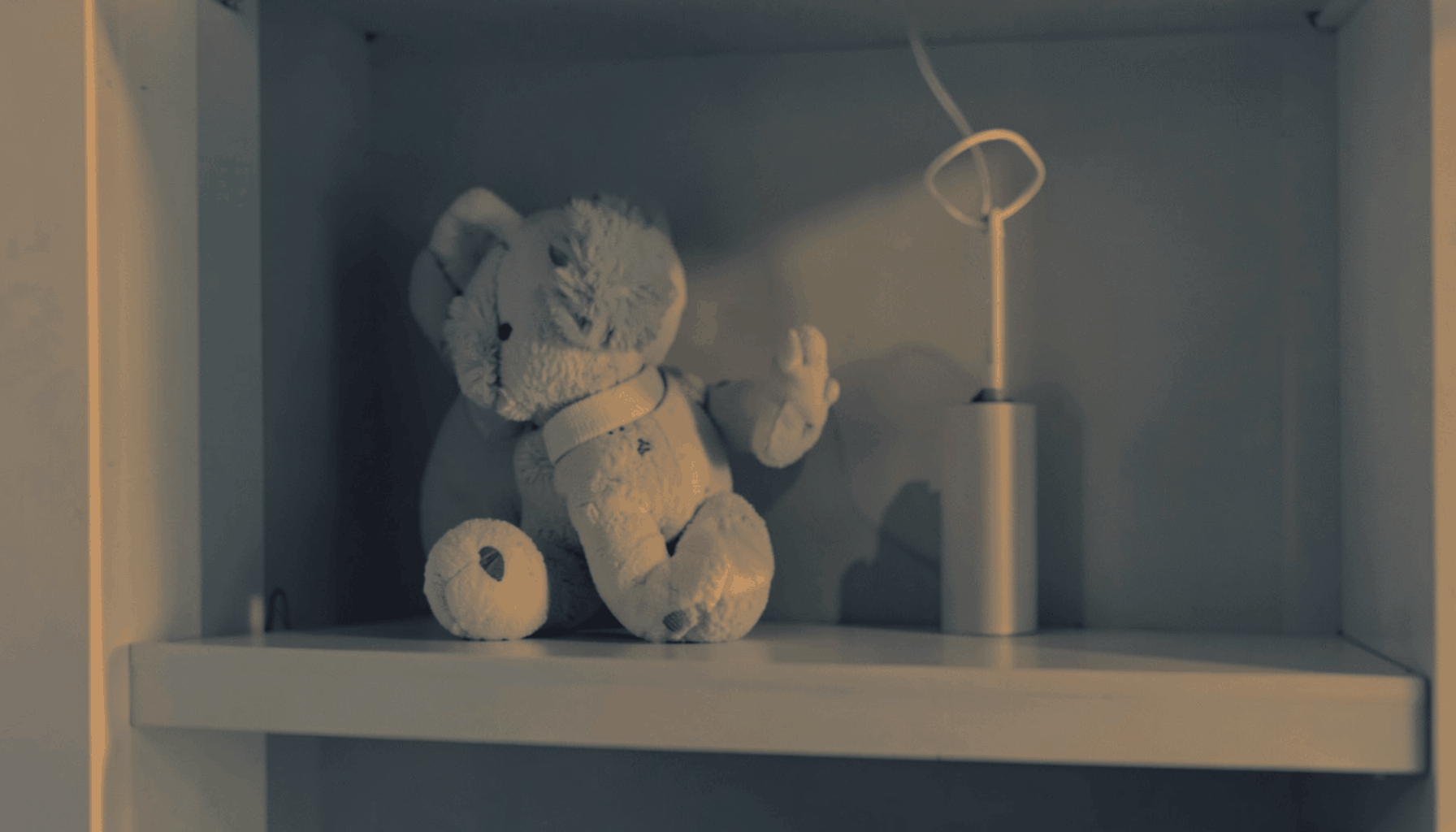 A warm duotone photograph of a parenting guide on a nursery shelf, in muted slate-blue and amber tones.