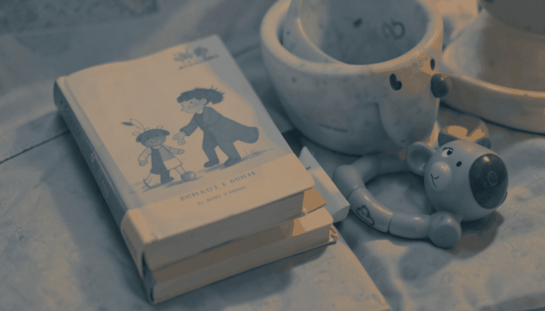 A warm duotone photograph of a parenting book next to a child's toy, in muted slate-blue and amber tones.